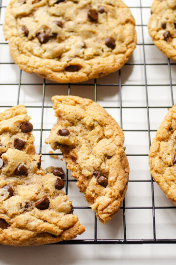 A hand holding a broken einkorn flour chocolate chip cookie on a wire cooling rack.