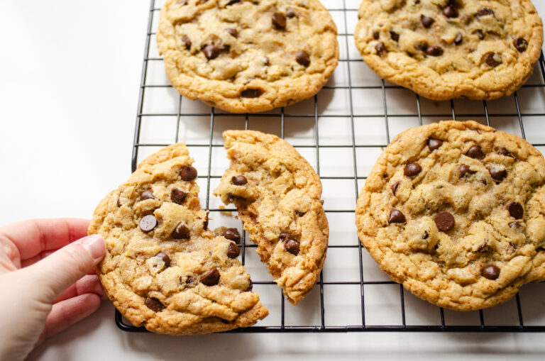 A hand holding a broken einkorn flour chocolate chip cookie on a wire cooling rack.