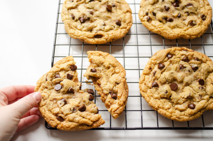 A hand holding a broken einkorn flour chocolate chip cookie on a wire cooling rack.