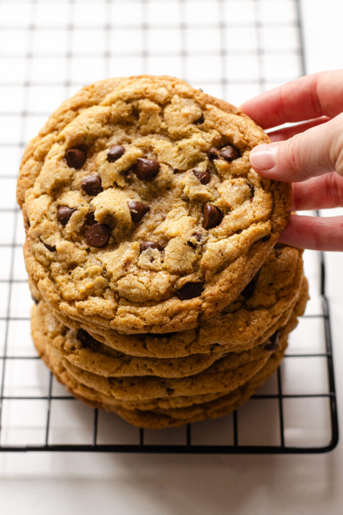 A hand holding up an Einkorn flour chocolate chip cookie on top of a stack of cookies.