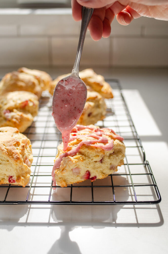 Drizzling the strawberry frosting on top of the cooled scones.
