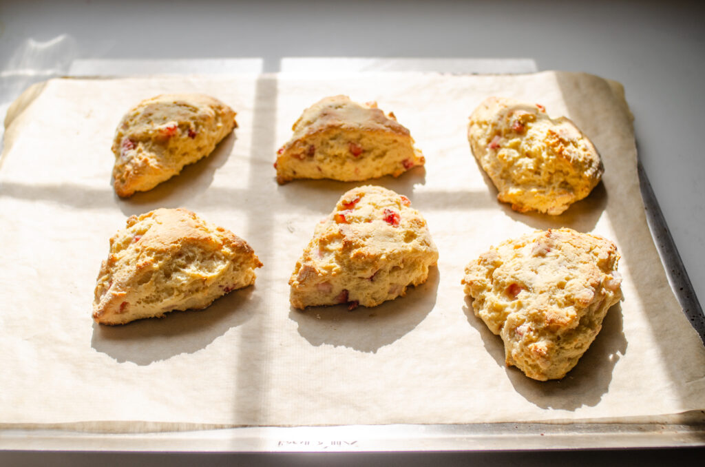 The baked strawberry scones on the baking sheet on a sunny couner.