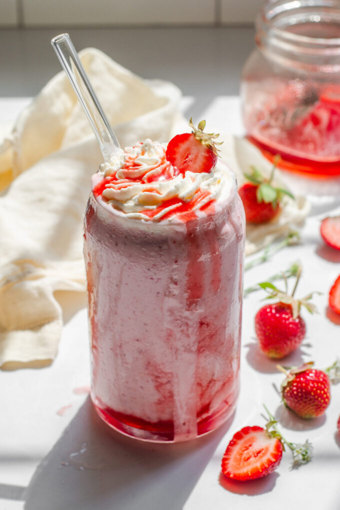 A strawberry milkshake made without ice cream on a white countertop with fresh strawberries to the side.