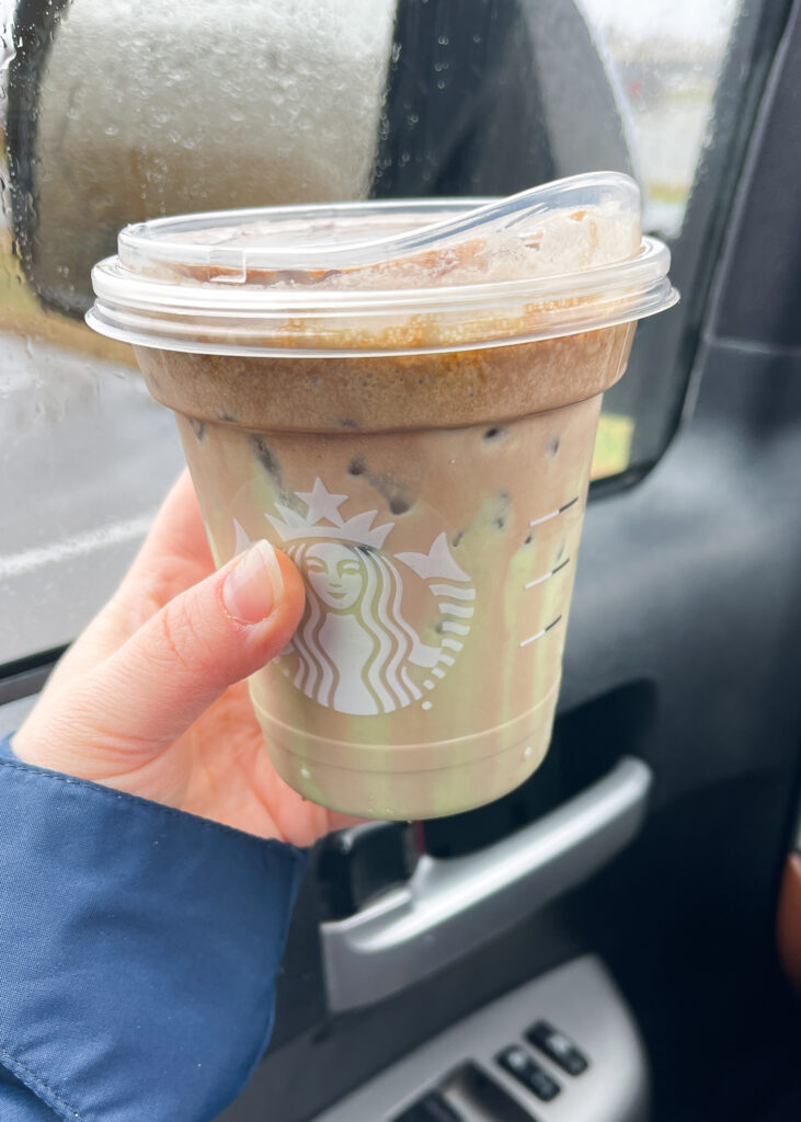 A hand holding the Starbucks Iced Dubai Chocolate Matcha in a car.