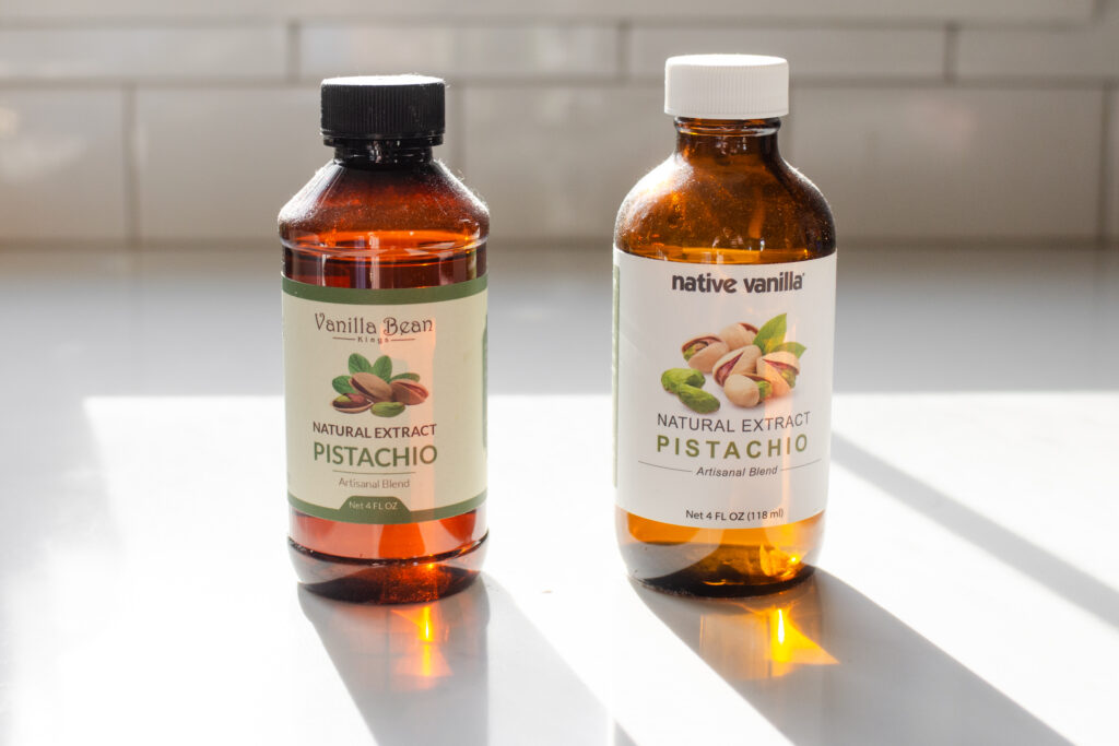 Two bottles of pistachio extract on a sunny white countertop.