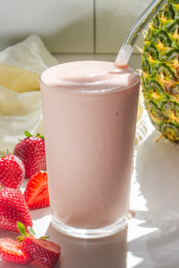 A strawberry pineapple smoothie with fresh strawberries on one side, and a whole pineapple in the background.