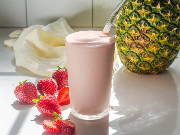 A strawberry pineapple smoothie with fresh strawberries on one side, and a whole pineapple in the background.