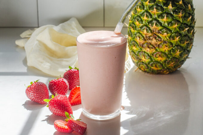 A strawberry pineapple smoothie with fresh strawberries on one side, and a whole pineapple in the background.