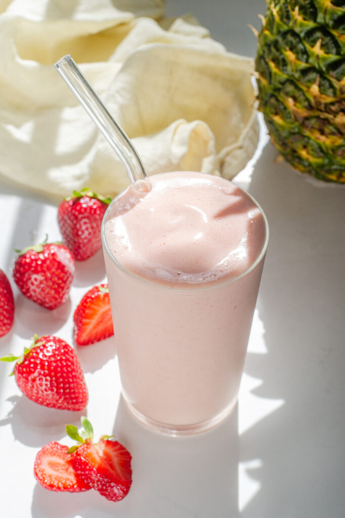 A strawberry pineapple smoothie with fresh strawberries on one side, and a whole pineapple in the background.