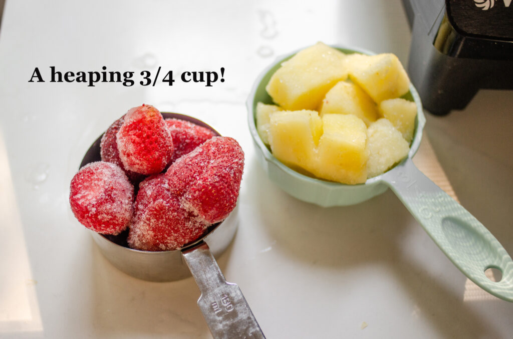 Measuring cups with frozen strawberries and pineapple showing how to measure a heaping cup.