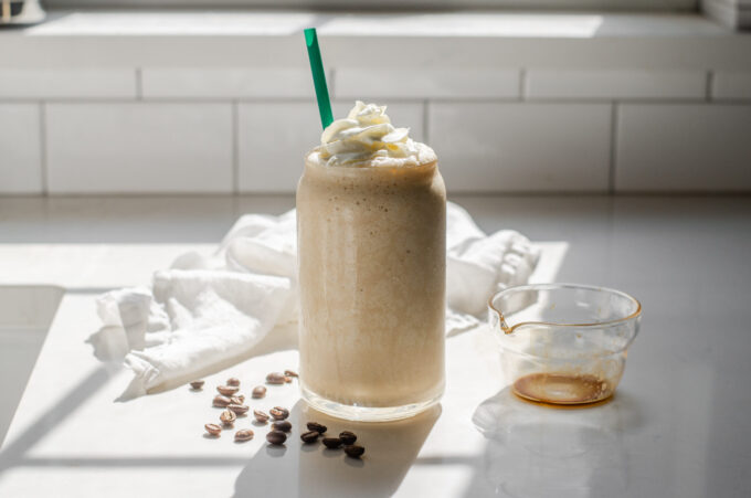 A Starbucks copycat Coffee Frappuccino in a glass cup on a white countertop with espresso beans on one side and a white napkin draped in the background.