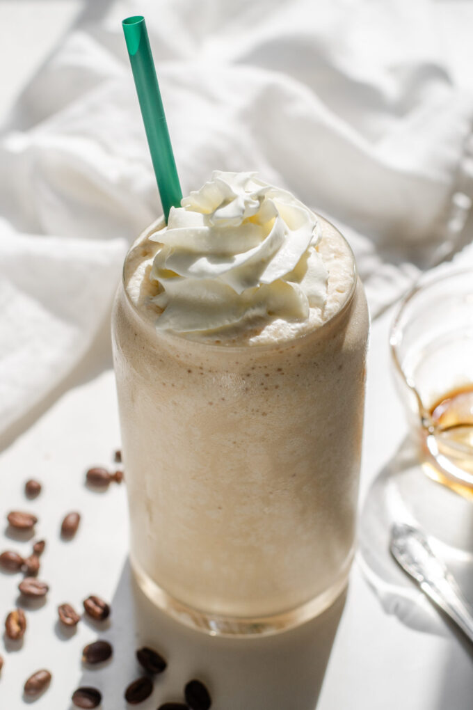 A Starbucks copycat Coffee Frappuccino in a glass cup on a white countertop with espresso beans on one side and a white napkin draped in the background.