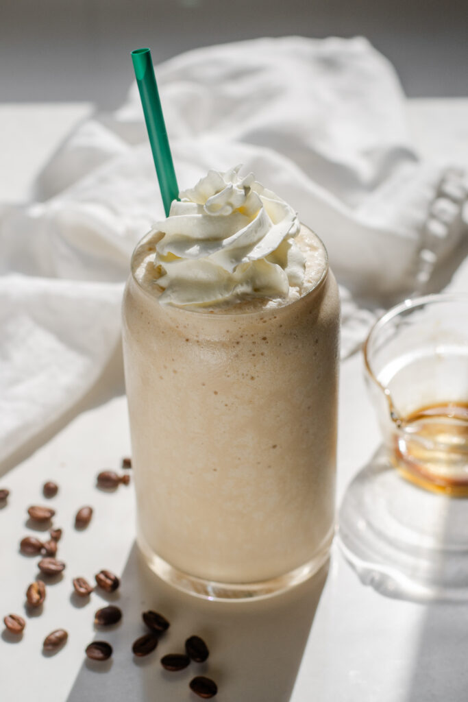 A Starbucks copycat Coffee Frappuccino in a glass cup on a white countertop with espresso beans on one side and a white napkin draped in the background.