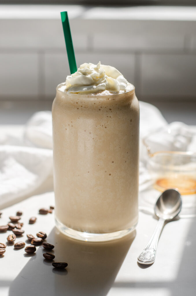 A Starbucks copycat Coffee Frappuccino in a glass cup on a white countertop with espresso beans on one side and a white napkin draped in the background.