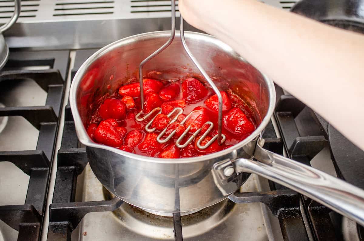 Mashing the strawberries with a potato masher as they begin to cook.