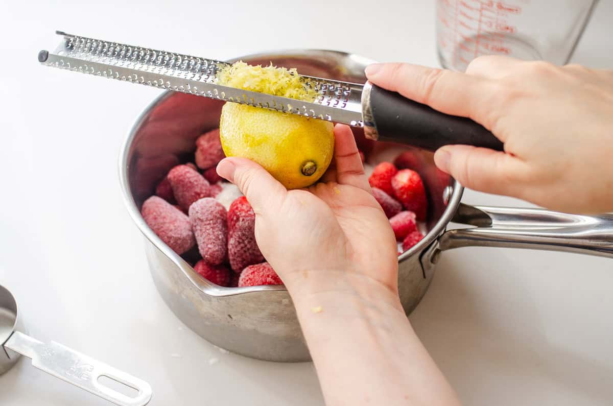 Zesting the lemon over the pot of frozen strawberries.