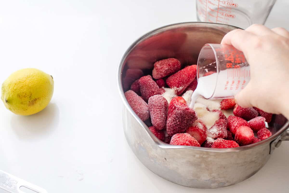 Pouring the cornstarch slurry over the frozen strawberries in the pan.