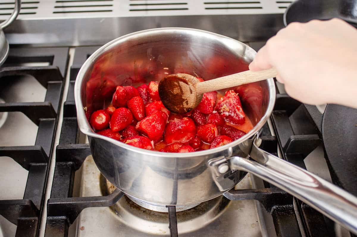 Stirring the strawberry sauce over the stove as it begins to cook.