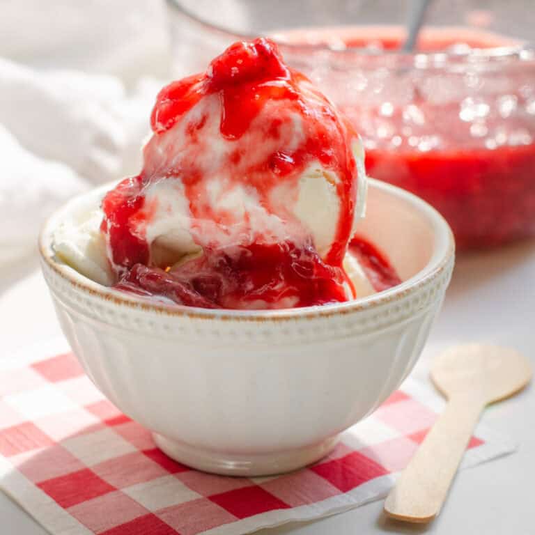 A bowl of ice cream on a gingham paper napkin with strawberry sauce on top.