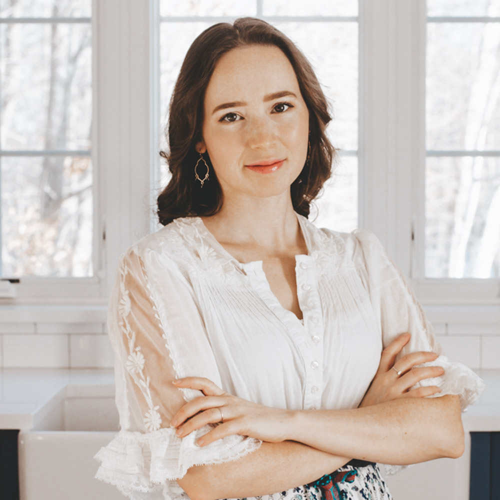 A woman in a white dress crossing her arms and looking at the camera.