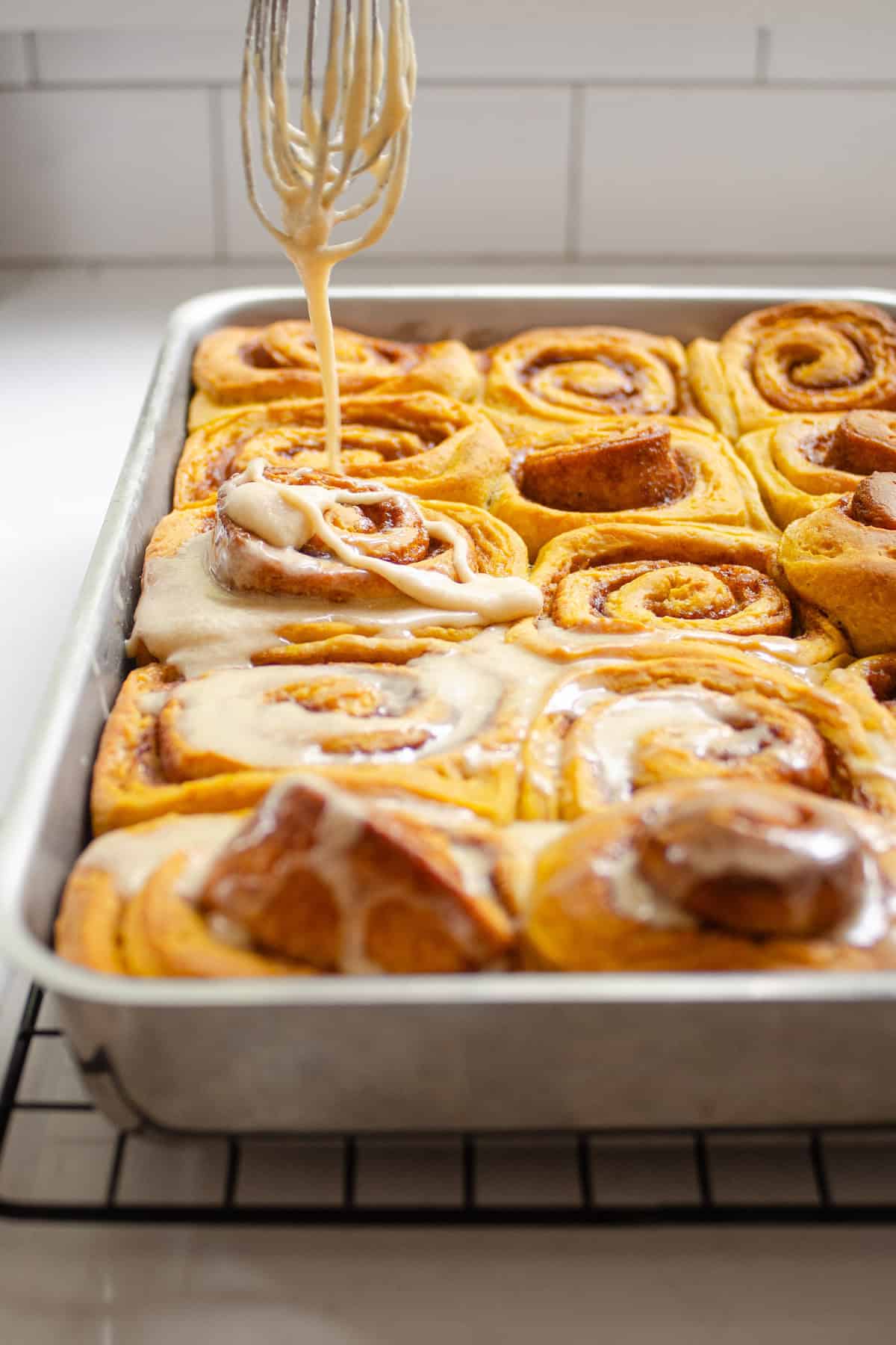 Drizzling the browned butter frosting on top of the sourdough pumpkin cinnamon rolls in the pan.