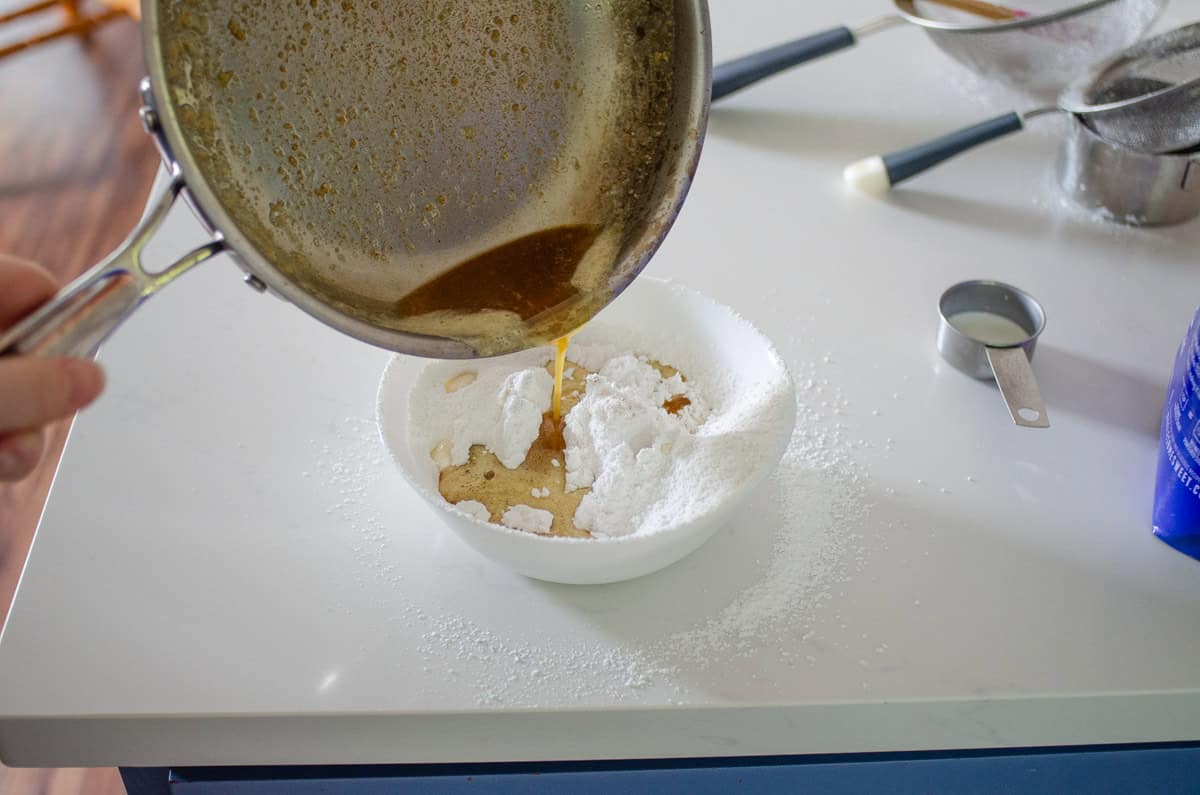Pouring browned butter into the bowl of sifted powdered sugar.