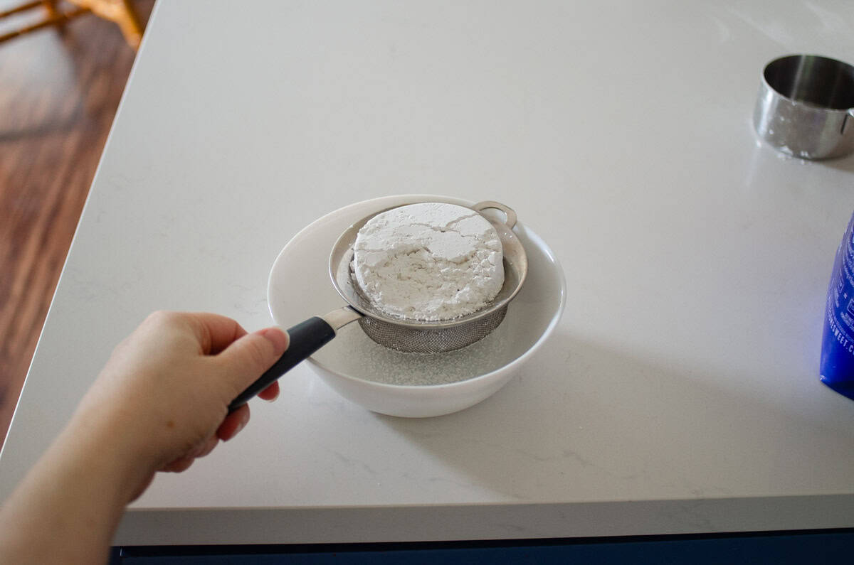 Sifting powdered sugar into a small bowl.