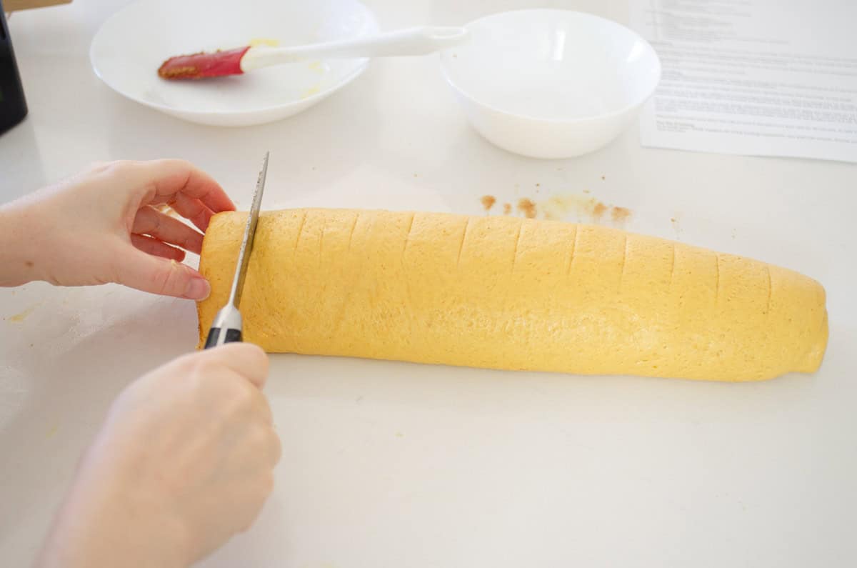Cutting the pumpkin cinnamon rolls with a serrated knife.