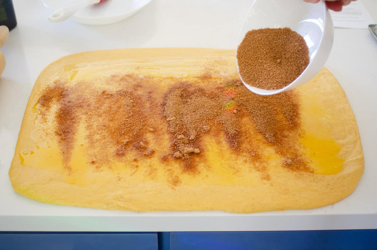 Sprinkling the cinnamon sugar mixture over the melted butter on top of the dough.