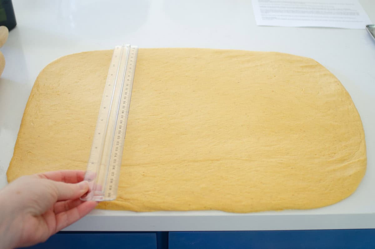 Measuring the pumpkin cinnamon roll dough to make sure the rectangle is the right size.