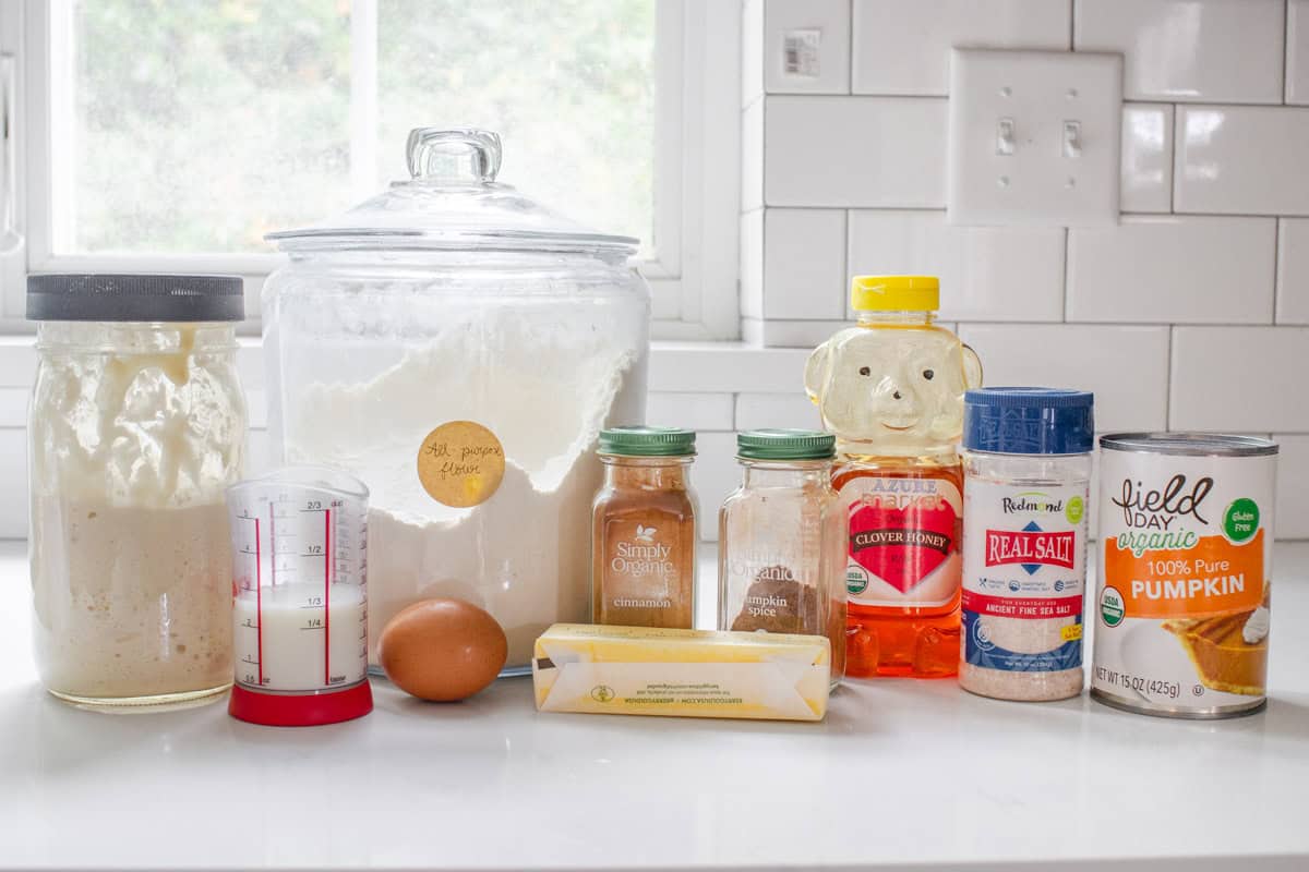 All of the ingredients needed to make sourdough pumpkin cinnamon rolls laid out on a white countertop.