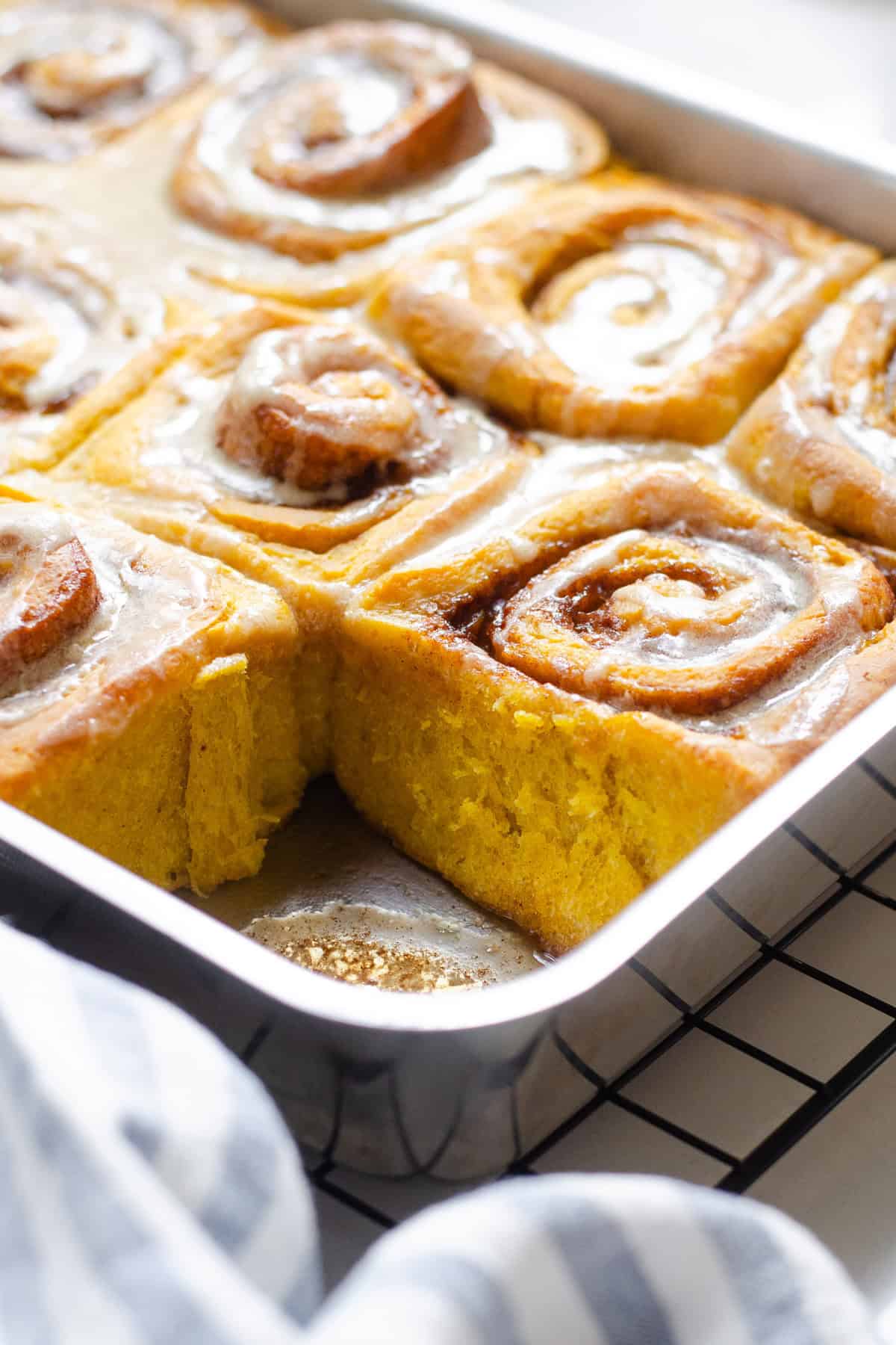 An angled photo of the pan of pumpkin cinnamon rolls with 1 roll taken out.